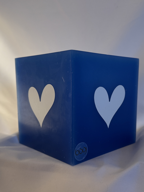 Photophore bleu à cœurs blancs – Collection boo-j Photophore bleu en cire minérale, cube d’environ 12 cm de côté, orné de deux cœurs blancs. Création artisanale boo-j, laissant passer la lumière avec douceur.