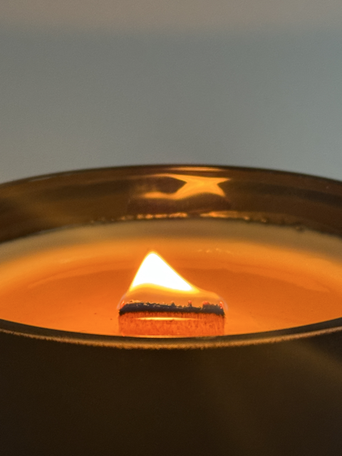 Bougie artisanale en cire végétale parfumée – mèche bois allumée Flamme allumée dans une bougie artisanale coulée à la main – cire lisse et chaude, mèche bois en combustion