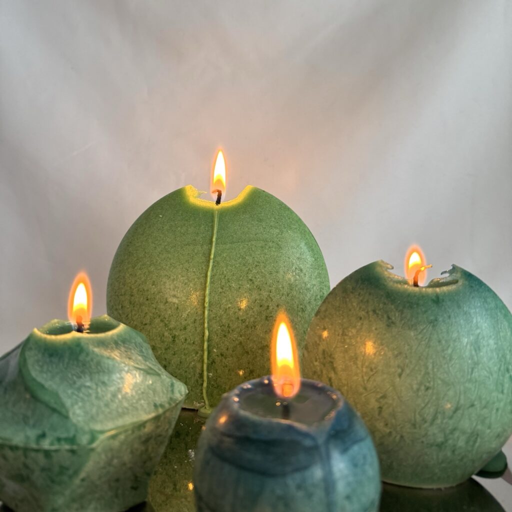 trois bougies en cire végétale allumées — tons vert de gris et vert profond