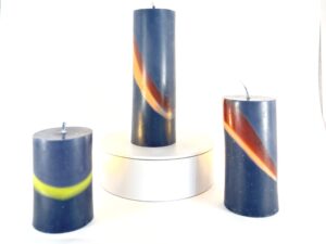 Trio de cylindres imparfaits en cire anthracite avec bandes colorées Trois bougies cylindriques en cire végétale teintée anthracite, traversées de bandes brun, orange et vert – série imparfaite et artisanale