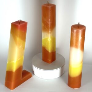 Photo de trois bougies artisanales en cire minérale – pilier, cylindre et 7UP – aux teintes orange, jaune, blanc et rouge