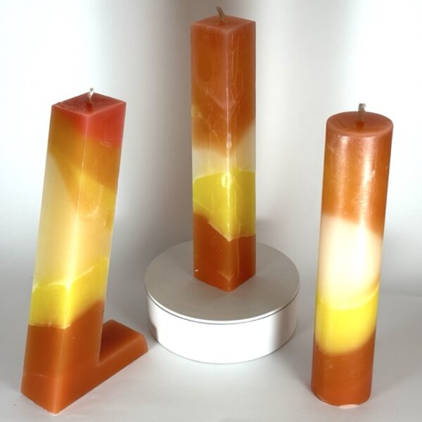 Photo de trois bougies artisanales en cire minérale – pilier, cylindre et 7UP – aux teintes orange, jaune, blanc et rouge