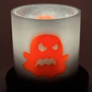 Photophore cylindre fantôme orange phosphorescent — boo-j | édition spectrale Photophore cylindrique Halloween en cire gris foncé, décoré d’un fantôme phosphorescent orange aux yeux en croix — boo-j édition spectrale