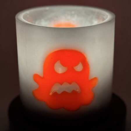 Photophore cylindrique Halloween en cire gris foncé, décoré d’un fantôme phosphorescent orange aux yeux en croix — boo-j édition spectrale