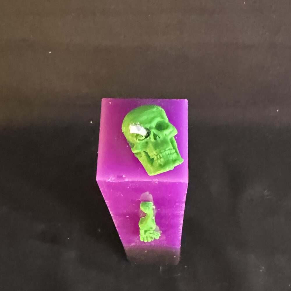 Bougie pilier Halloween violette en cire minérale et végétale, décorée d’un crâne et d’os en cire d’abeille vert fluo — création artisanale suisse boo-j, édition spectrale