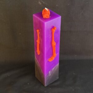 Bougie pilier 5 × 21 cm violette — crâne et os en cire d’abeille orange | boo-j édition spectrale Bougie pilier Halloween violette en cire minérale et végétale, décorée d’un crâne et d’os en cire d’abeille orange vif — création artisanale suisse boo-j, édition spectrale