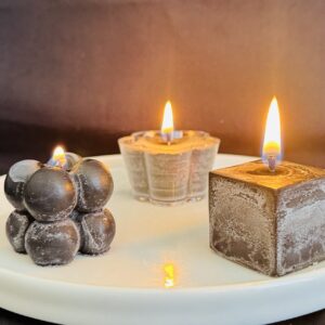 Bougies artisanales allumées — collection Pierre de Volcan, cire stéarine végétale, finitions noires et grises texturées.