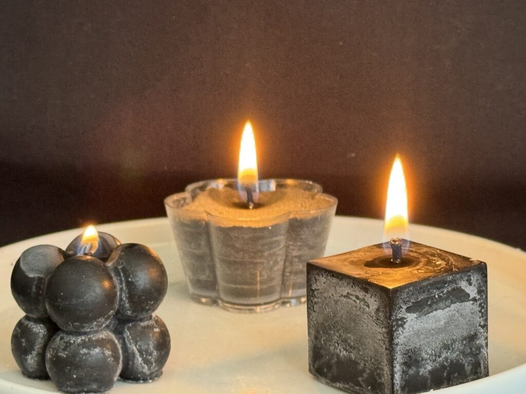 Bougies artisanales allumées — collection Pierre de Volcan, cire stéarine végétale, finitions noires et grises texturées.