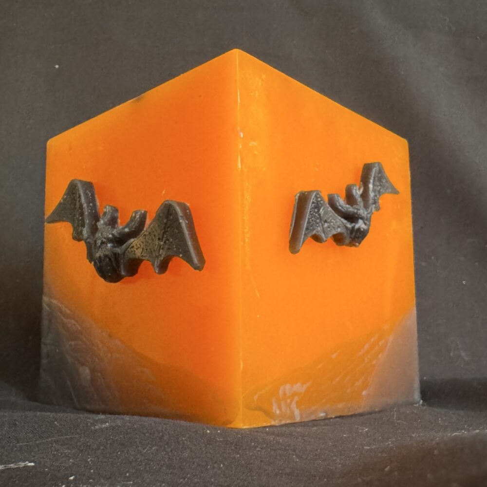 Bougie cubique Halloween de 10 cm, ± 700 g, en cire minérale et végétale orange avec chauves-souris en cire d’abeille noire — création artisanale suisse boo-j, édition spectrale