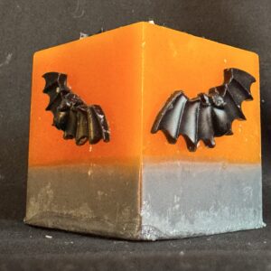 Bougie cube 5 cm Halloween — décorations en cire d’abeille noire | boo-j édition spectrale Bougie cubique Halloween de 5 cm, environ 120 g, en cire minérale et végétale orange, décorée de chauves-souris en cire d’abeille noire — création artisanale suisse boo-j, édition spectrale