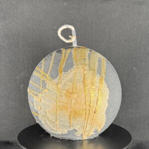 Bougie artisanale en forme de disque gris avec coulures dorées, réalisée à la main en cire végétale. Création boo-j fabriquée dans le canton de Vaud.