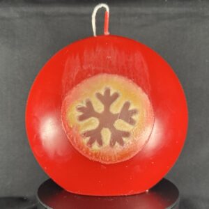 Bougie artisanale rouge et dorée avec motif central de flocon blanc, coulée à la main en cire minérale et végétale. Création boo-j, fabriquée dans le canton de Vaud.