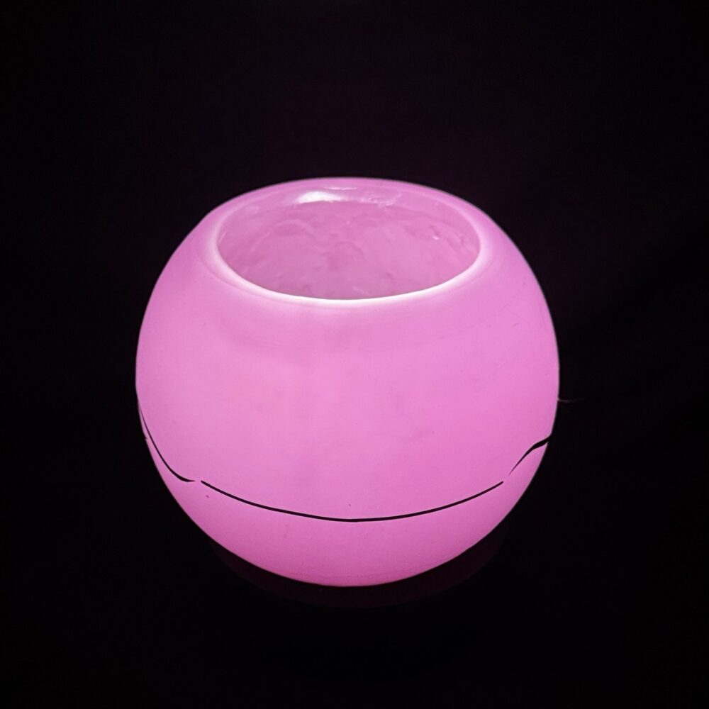 Photophore sphérique rose en cire minérale translucide, décoré d’un motif de vagues noires, fait main dans le canton de Vaud.
