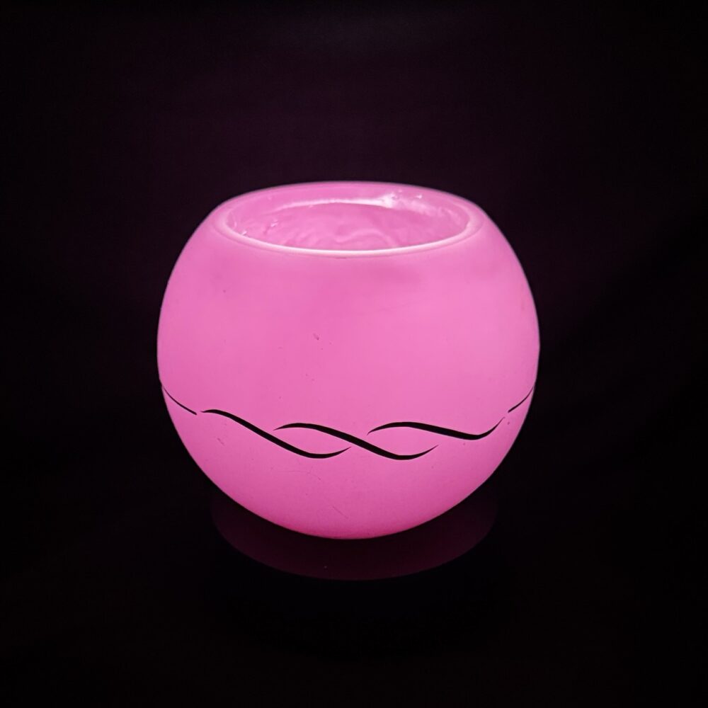 Photophore sphérique rose en cire minérale translucide, décoré d’un motif de vagues noires, fait main dans le canton de Vaud.
