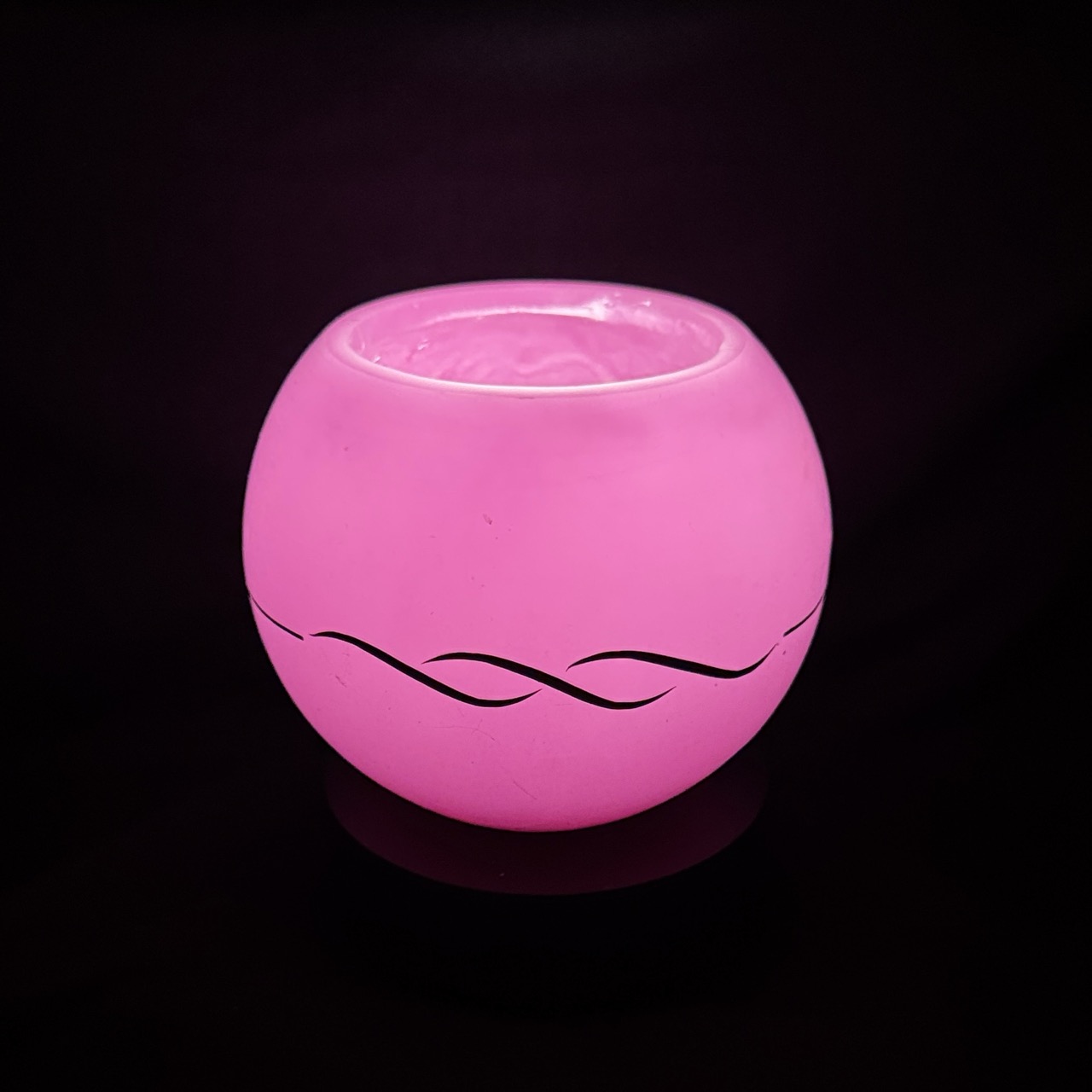 Photophore sphérique rose en cire minérale translucide, décoré d’un motif de vagues noires, fait main dans le canton de Vaud.